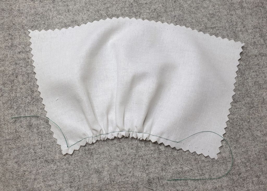 Fotografi av at en prøvelapp er sydd med lange sting på symaskin. Etterpå er det dratt i tråden, slik at stoffet rynker seg. 