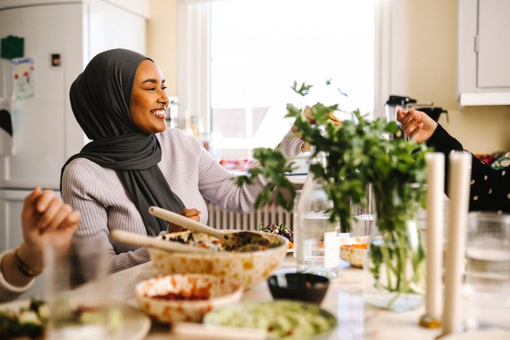 Smilende afrikansk kvinne sitter ved et bord med flere matretter. Foto.
