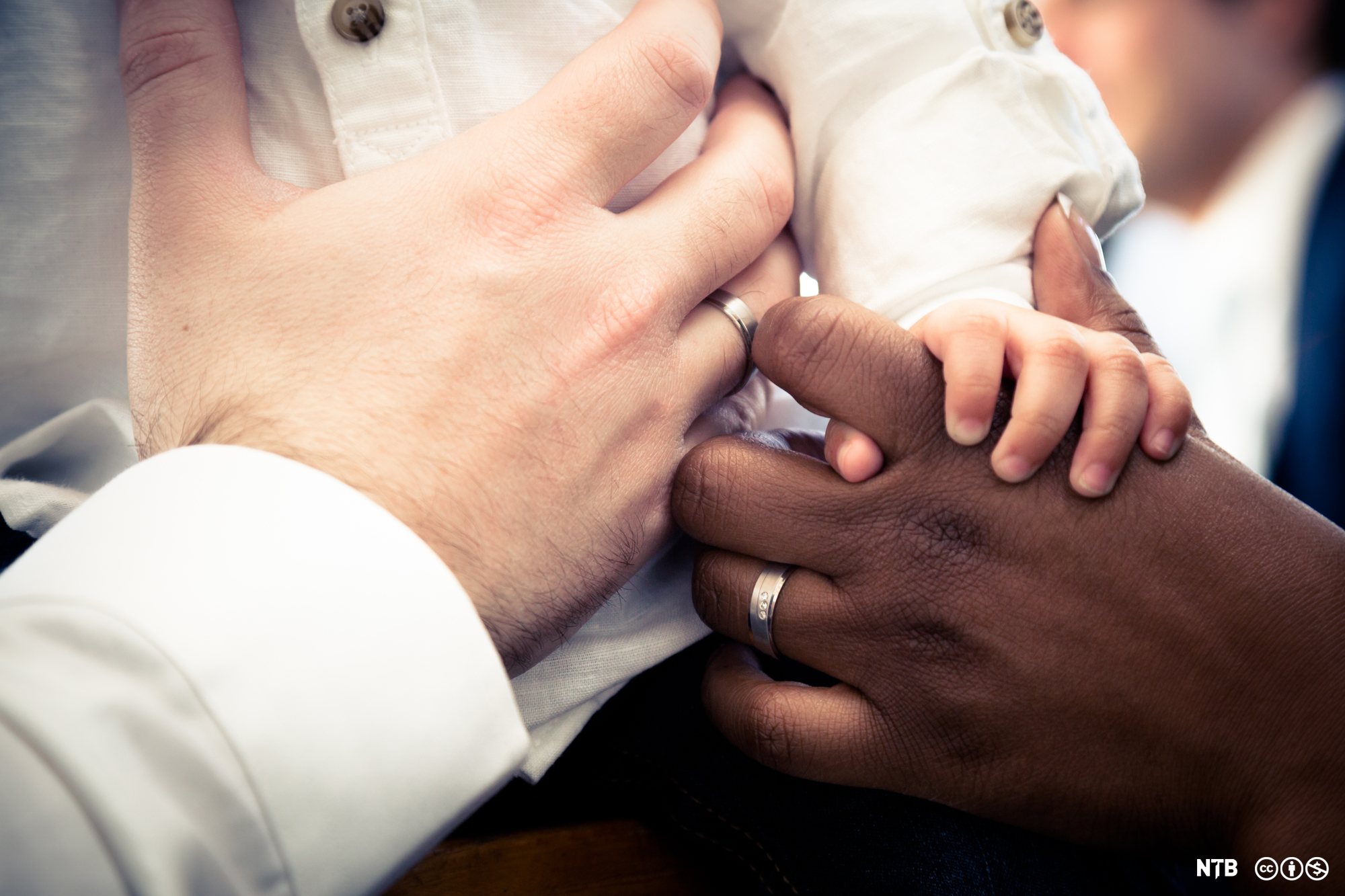 A photo showing only the hands of a Black woman, a white man, and their baby.  