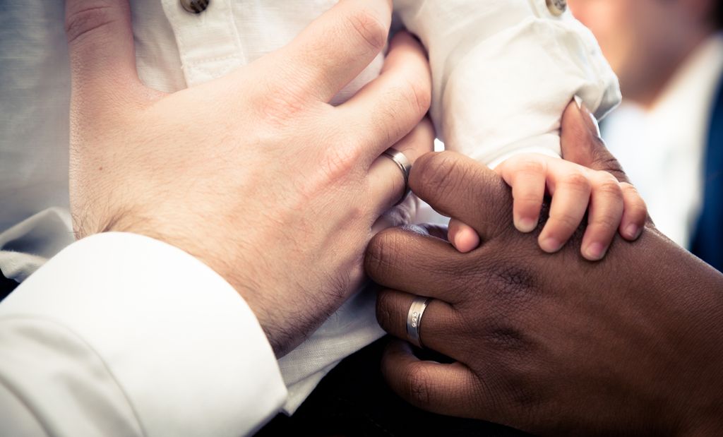 A photo showing only the hands of a Black woman, a white man, and their baby.
