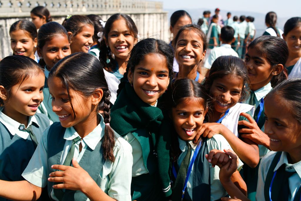 Group picture of Indian school girls, all smiling and laughing. They are wearing school uniforms. Photo.