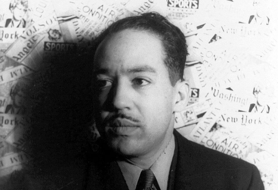 Langston Hughes is a middle aged man. He is wearing a suit. He has a thin moustach. Photo.