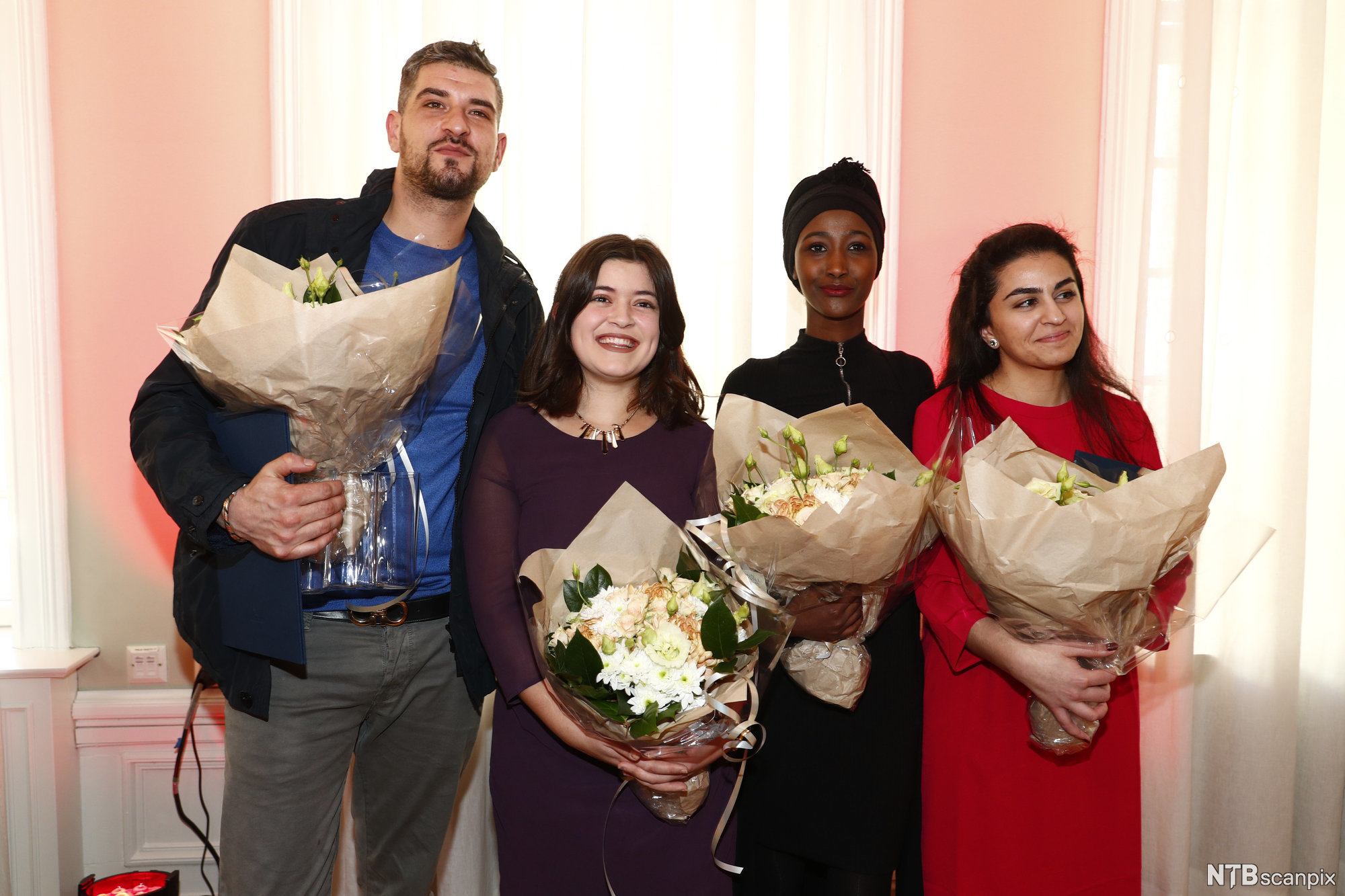 Foto av en mann og tre unge kvinner med minoritetsbakgrunn. Alle fire holder hver sin blomsterbukett etter å ha fått en pris. 