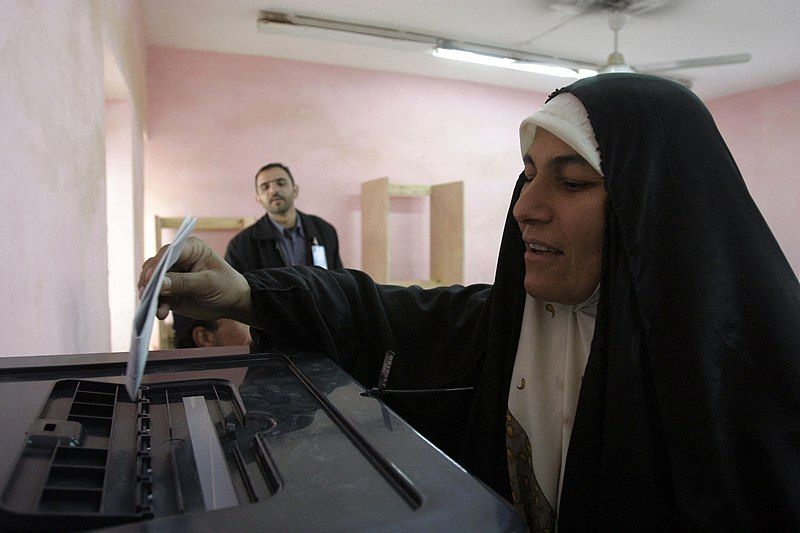 An Iraqi woman prepares to cast her ballot. A man is watching in the background. Photo.