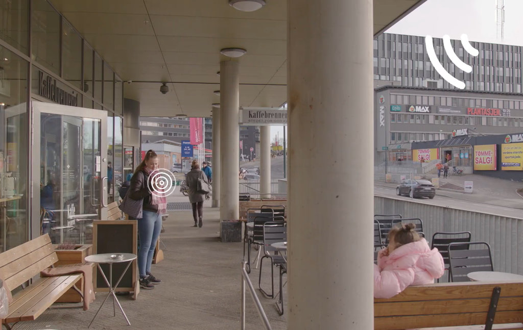 Skjermdump fra film om radiosignaler. Jente står med mobil i et bymiljø, og det går animerte signaler fra mobilen til basestasjonen på toppen av en bygning. Foto.