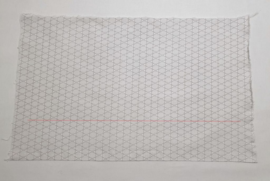 Fotografi av tøystykke der trådretningen er markert med en rød strek.