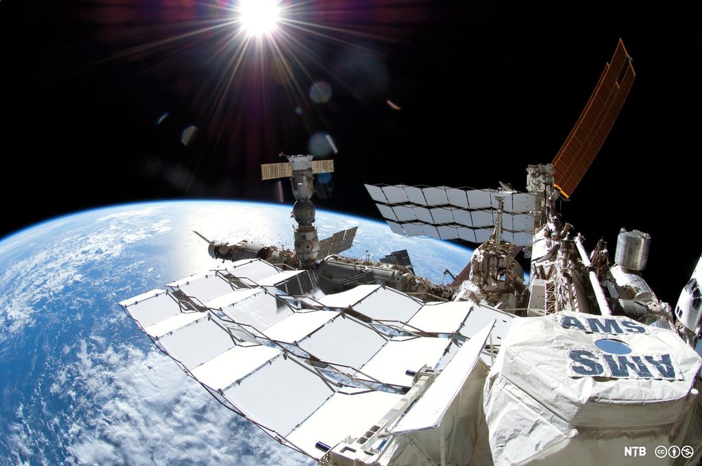 The Earth beneath a satellite structure. The structure is white. The letters AMS are seen on one part of the structure. Photo.