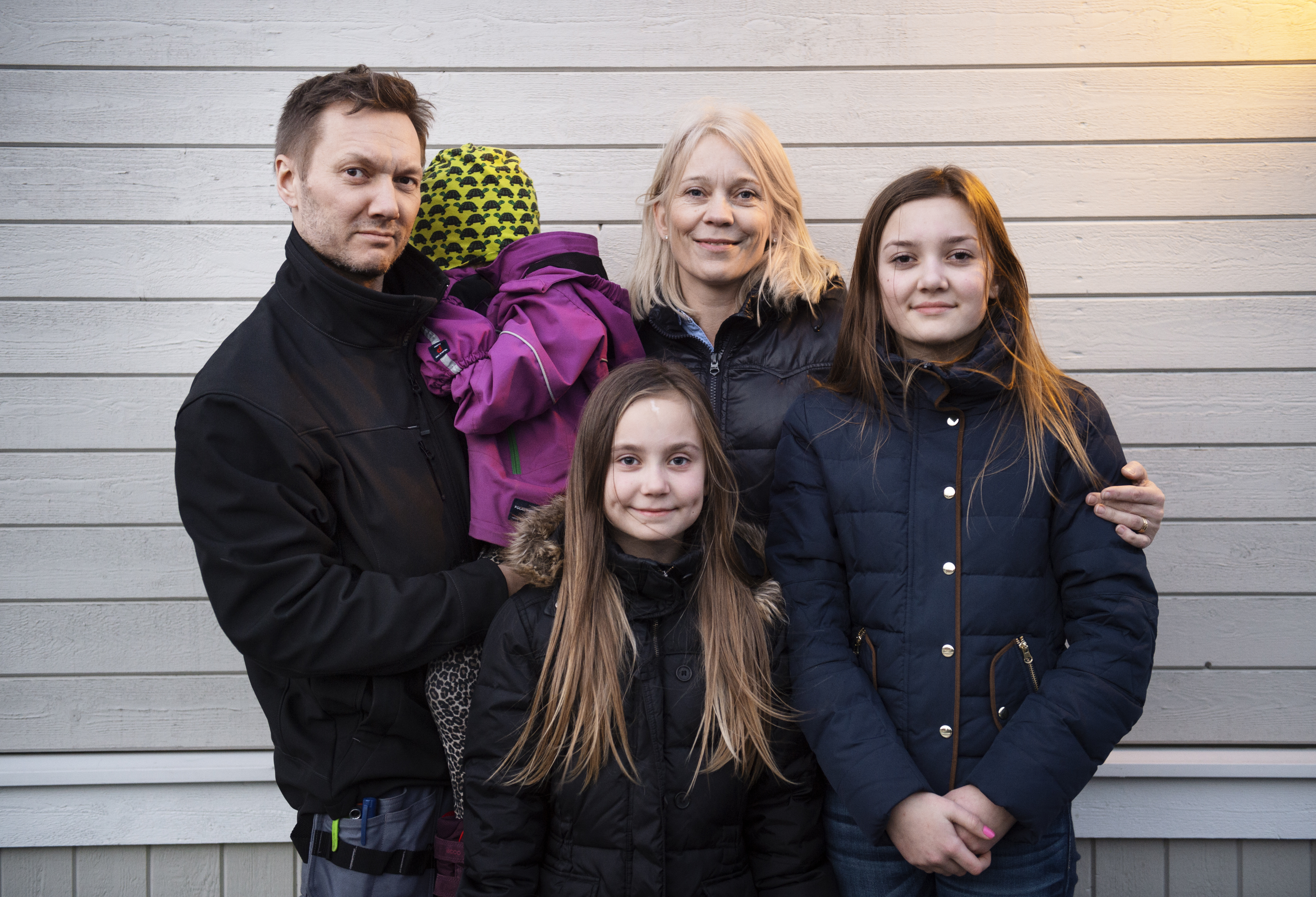 Mann, kvinne og tre barn i boblejakker foran en vegg med liggende bordkledning. Ett av barna er tenåring, ett er i barneskolealder og ett er i barnehagealder. Foto.