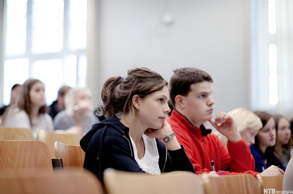 Studentar sit på rekke og rad i eit auditorium. Foto. 