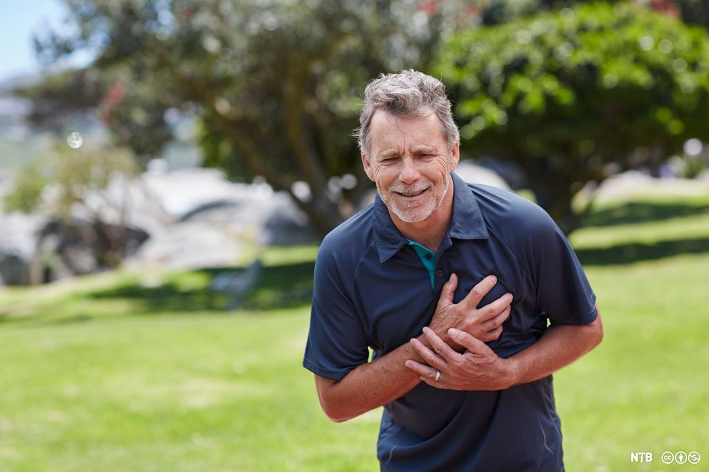 En eldre mann som holder hendene foran brystet og bøyer seg framover med et plaget uttrykk i ansiktet. Foto.