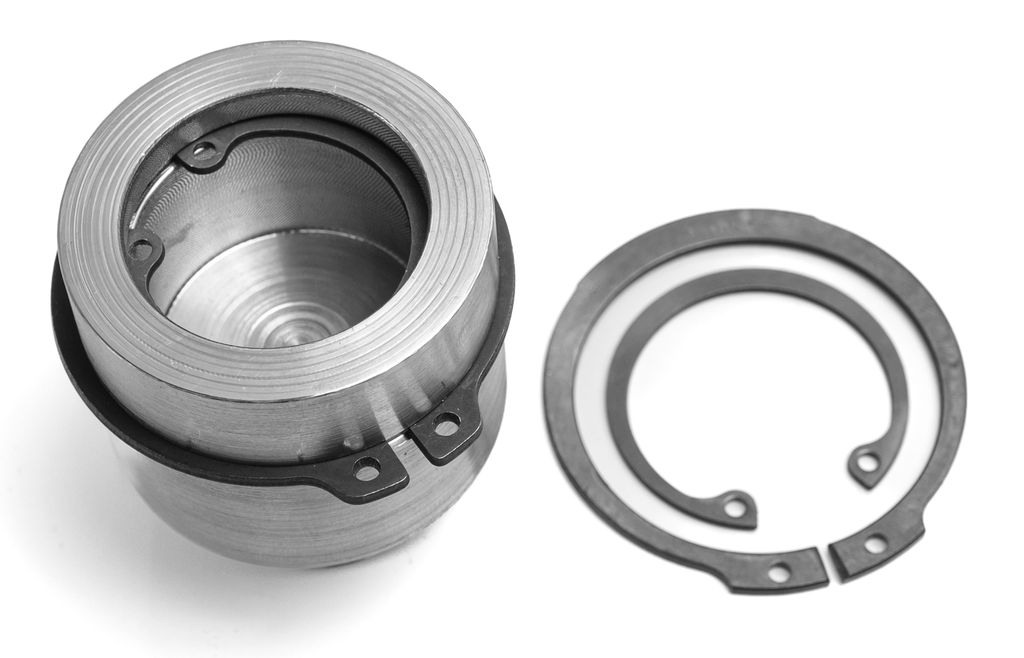 Metallsylinder med stålringer rundt. To stålringer ligger ved siden av. Foto.