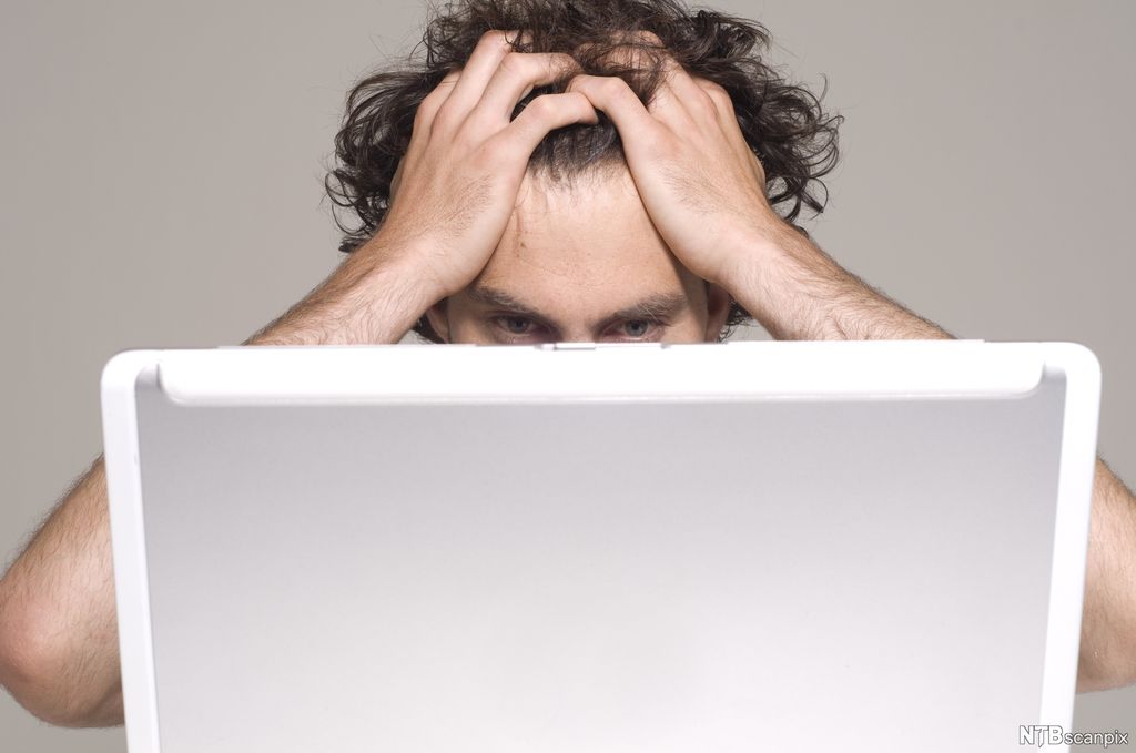 En mann tar seg til håret foran en dataskjerm. Foto.