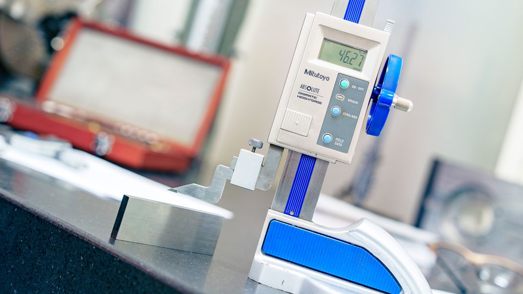 Måleverktøy står på et bord med målespissen løfta fra bordet. Skjermen viser verdien 46,27. Foto.