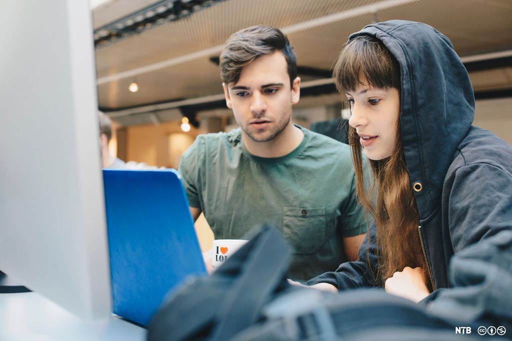 To personer sitter foran laptop og studerer skjermen. Foto.