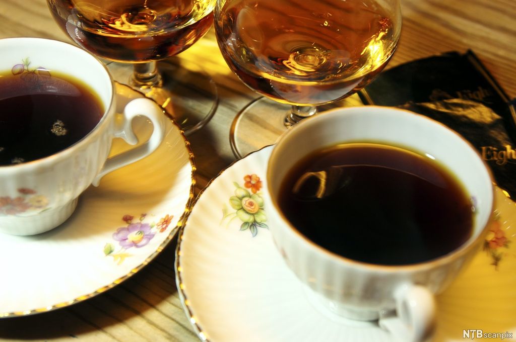 To pene kaffekopper med kaffe og to konjakkglass med konjakk som står ved siden av hverandre på et bord. Foto.