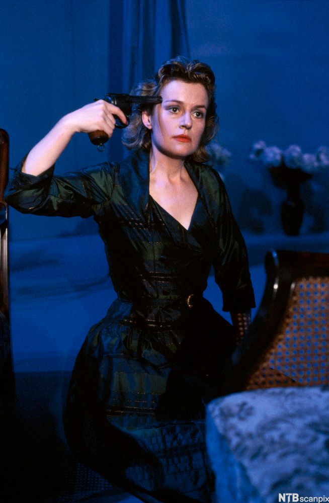 Bilde av skuespiller Catherine Wilkin i rollen som Hedda Gabler. Hedda er kledd i sort og holder en pistol mot tinningen sin. Fra Downstage Theatre Company's produksjon av Ibsens Hedda Gabler (1990). Foto. 