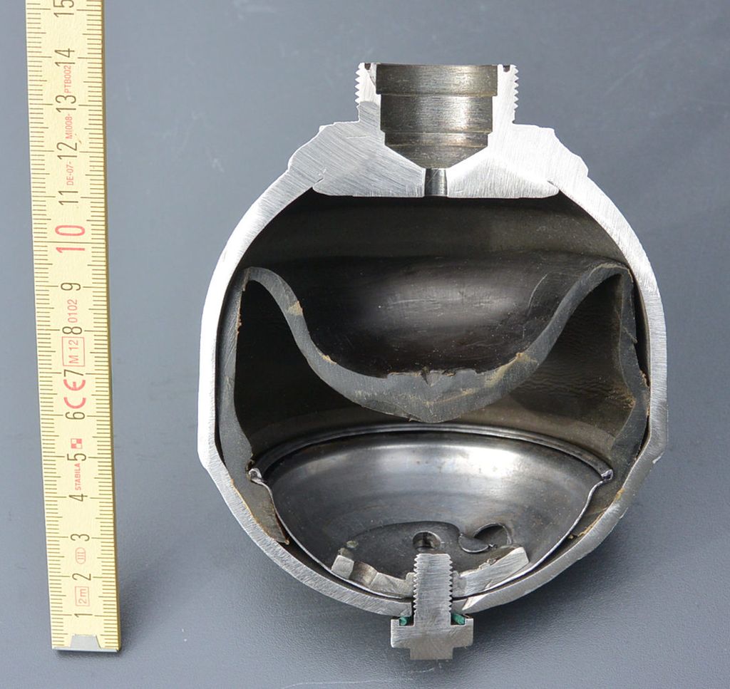 Gjennomskåret trykkakkumulatortank. To kamre er delt med en gummimembran. En tommestokk ved siden av viser at høyden er 14 cm. Foto.