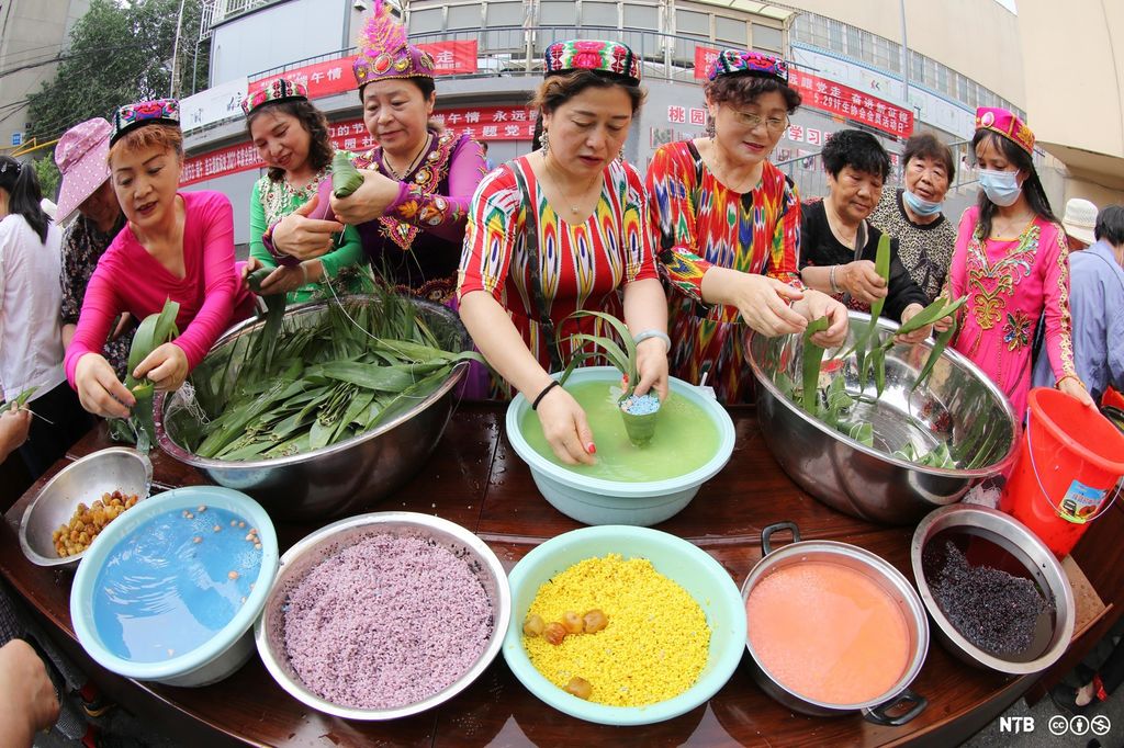 Seven women of Asian origin are preparing food. In front of them are bowls filled with food in many different colours. Photo.