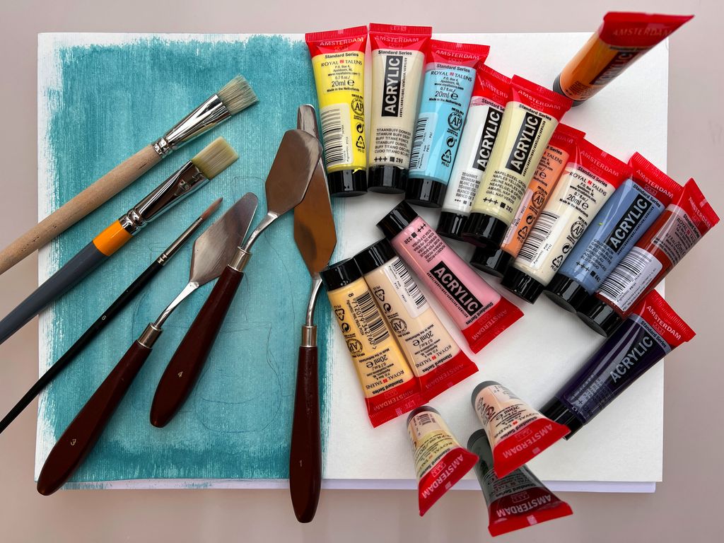 Utstyr til akrylmaling ligger oppå et delvis grunnet papir. Foto.