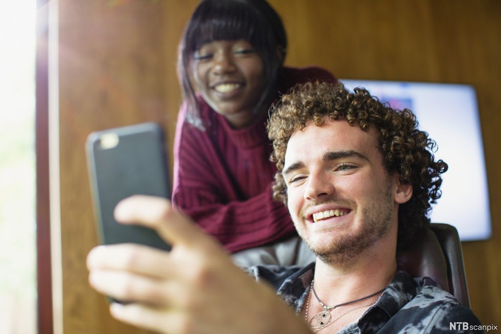 To ungdommer ser på en mobil og ler. Foto.