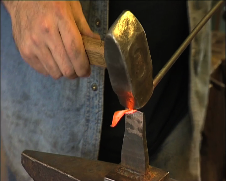 Hånd med hammer som jobber med glødende metall. Foto.