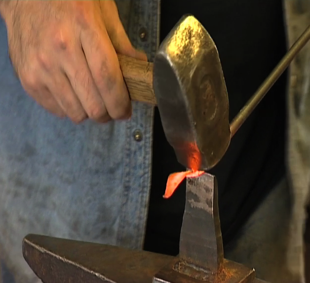 Hand som hamarar på glødande metall. Foto.