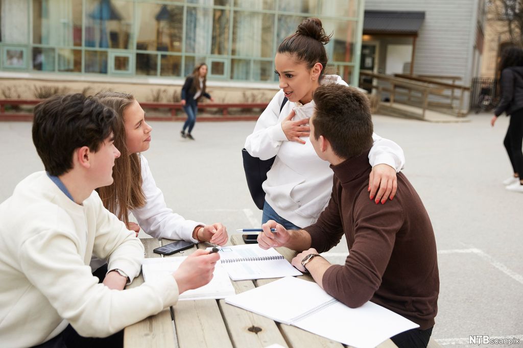 Fire ungdommer snakker rundt et bord. Ei av jentene står og holder rundt skuldrene til den ene gutten. De andre følger interessert med i samtalen. Foto.