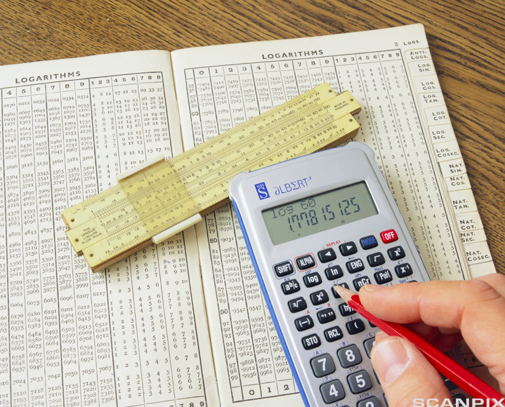 Regnestav og kalkulator på en oppslått logaritmetabell. Ei hånd bruker en blyant til å trykke på knappene på kalkulatoren. Foto.