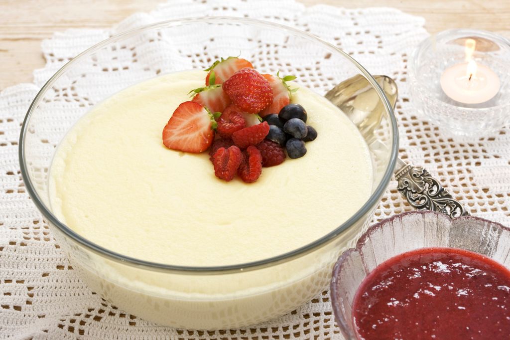 Fløterand i en serveringsbolle, pyntet med jordbær, bringebær og blåbær. Rød saus servert i skål ved siden av. Foto.