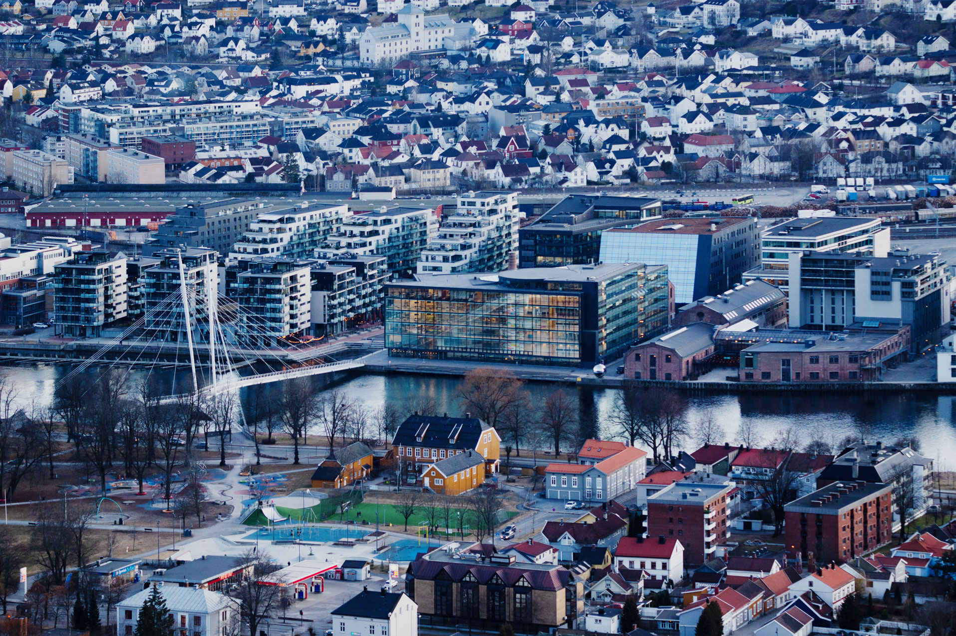 Tettbygd byområde med ei elv som går horisontalt midt i biletet. Det går ei bru over elva, og det er fleire nye bygg på den eine sida av elva. Foto.