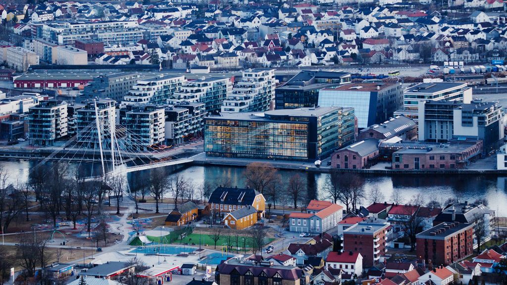 Tettbygd byområde med ei elv som går horisontalt midt i biletet. Det går ei bru over elva, og det er fleire nye bygg på den eine sida av elva. Foto.