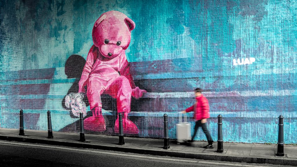 Ein stor rosa teddybjørn sit på ein kant og held ein bukett blomstrar. Foto.