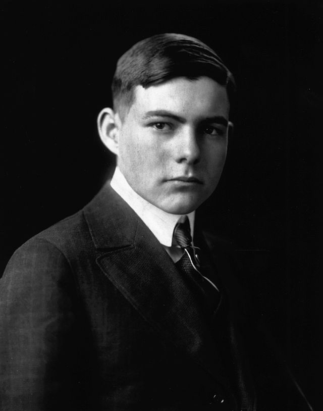 Photo: Portrait of Ernest Hemingway. We see a young, dark-haired man. He is wearing a suit and tie. 