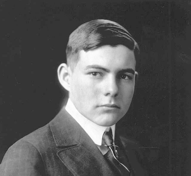 Photo: Portrait of Ernest Hemingway. We see a young, dark-haired man. He is wearing a suit and tie.