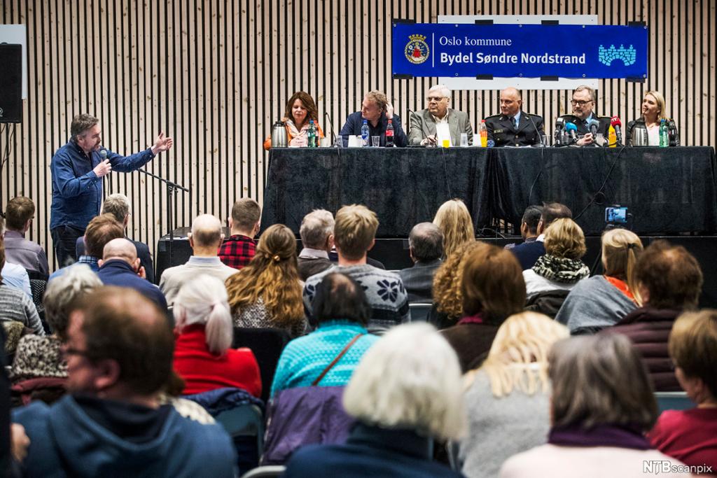 Folkemøte på Holmlia etter ein skyteepisode. Politi og nasjonale og lokale politikarar på podiet. Foto. 