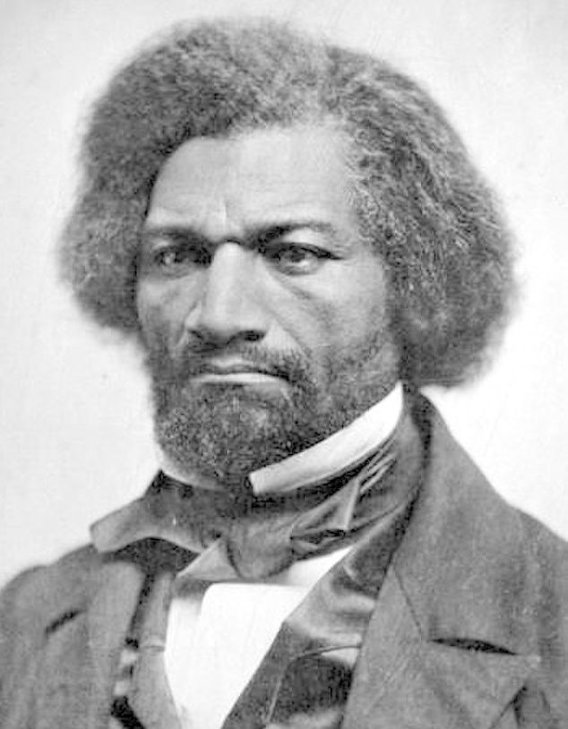 A black and white photo of Fredrick Douglass. He is a Black man dressed in a suit and a bow. He has thick hair and a beard. His expression is sad, or even angry.