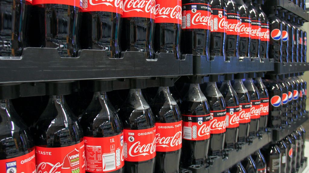 Store flasker med Coca Cola og Pepsi på paller i en butikk. Foto.