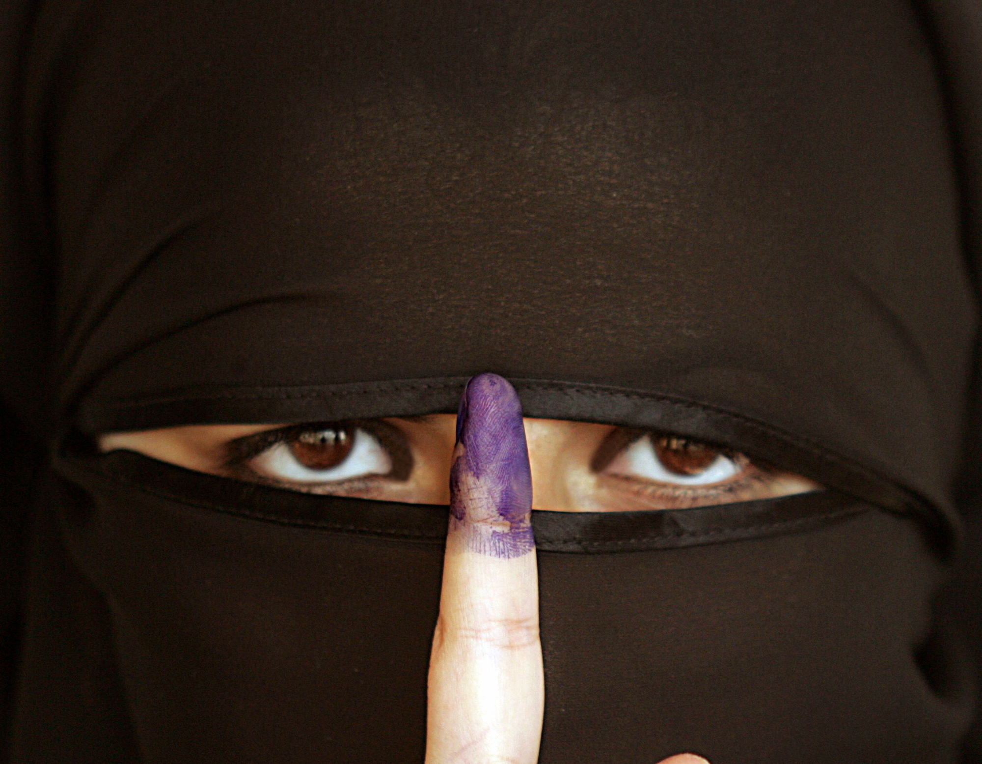 Kvinne iført nikab holder opp en pekefinger med blekk på. Foto.