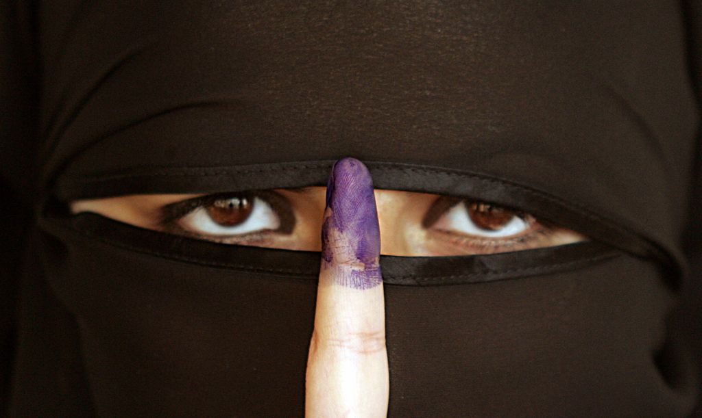 Kvinne iført nikab holder opp en pekefinger med blekk på. Foto.