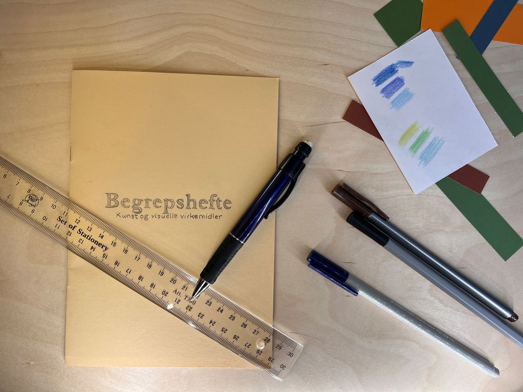 Tittelsida til begrepsheftet og tegnesaker på arbeidsbordet. Foto.