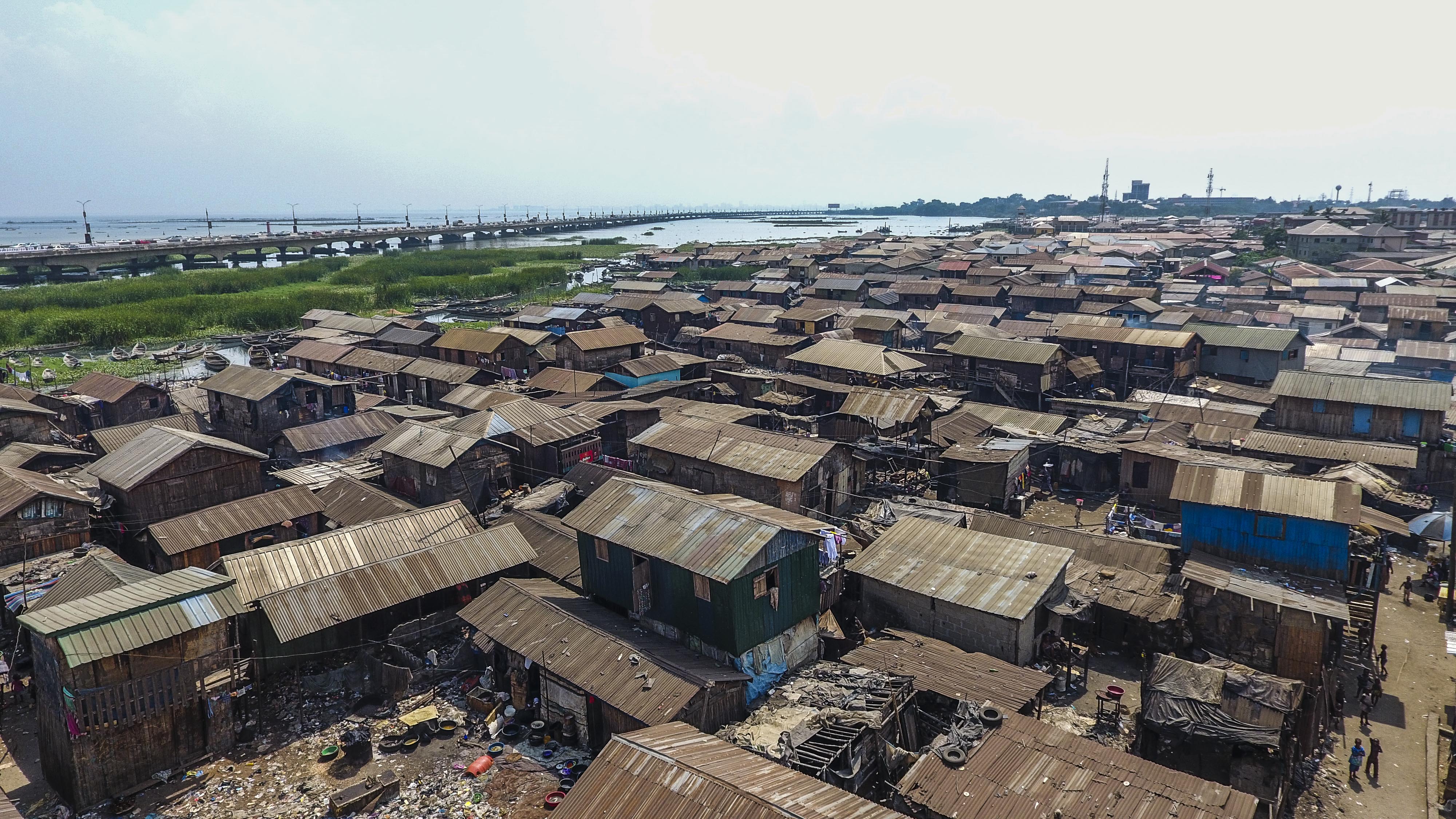 Mange hus av dårlig kvalitet og med blikktak tett i tett. En motorvei i bakgrunnen. Foto. 