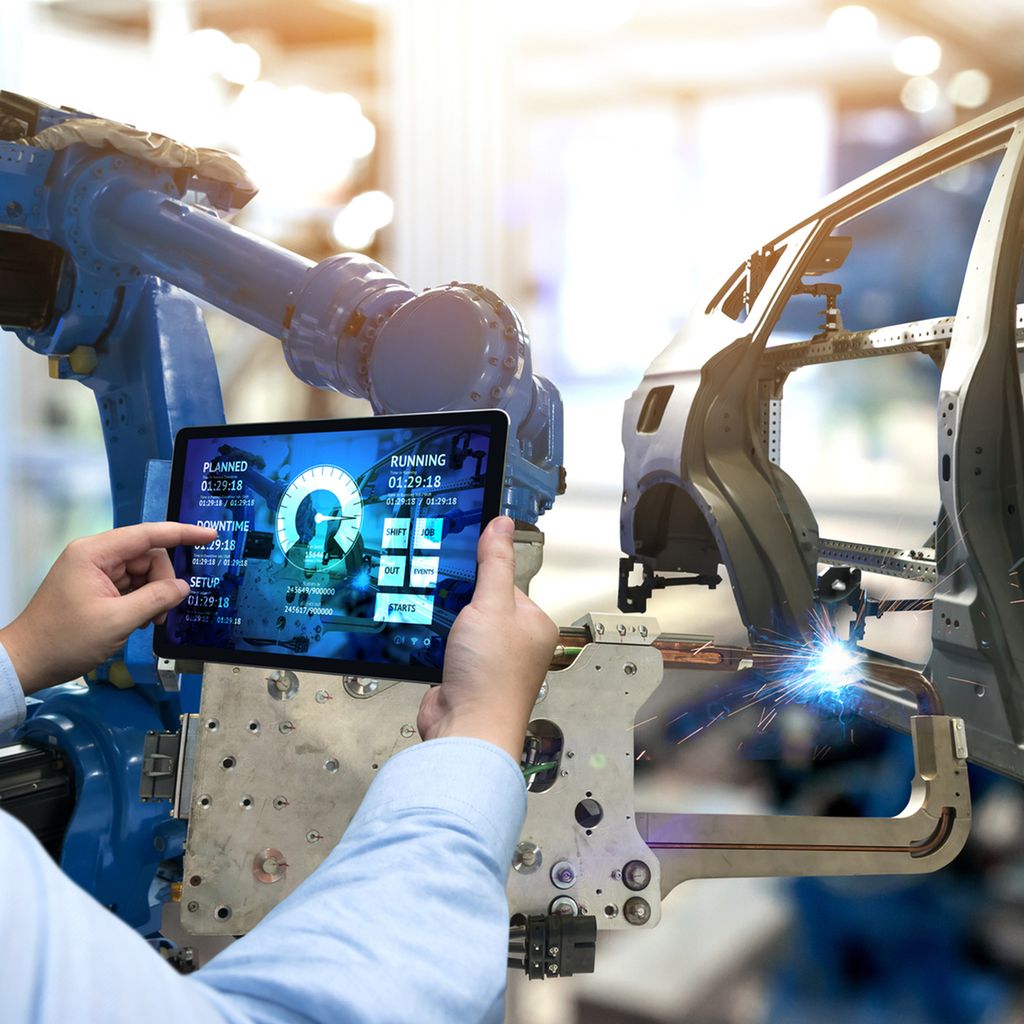 Hender som betjener en skjerm som styrer en sveiserobot. Foto.