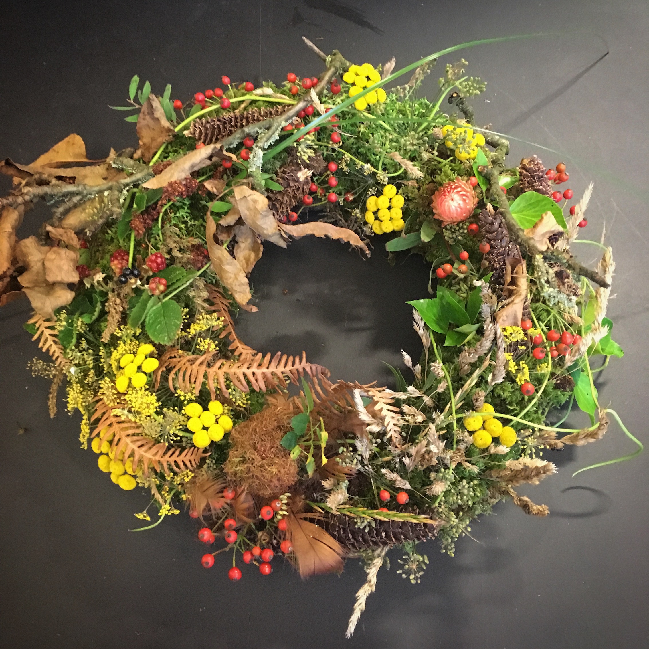 Blomsterkrans med bær, blader, kongler og blomster. Foto.