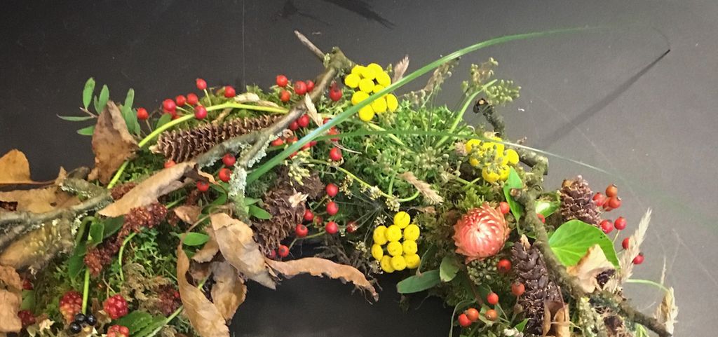 Blomsterkrans med bær, blader, kongler og blomster. Foto.