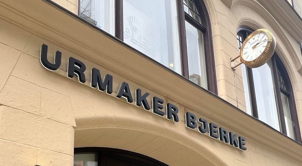 Bygningsfasade i mur. Over en inngangsdør står det Urmaker Bjerke med store bokstaver. Foto.