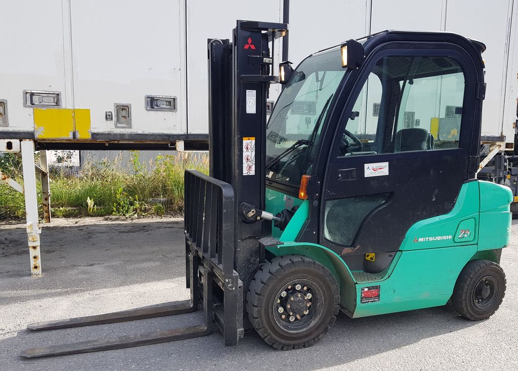 Grønn motvektstruck parkert ved en hvit container. Foto.