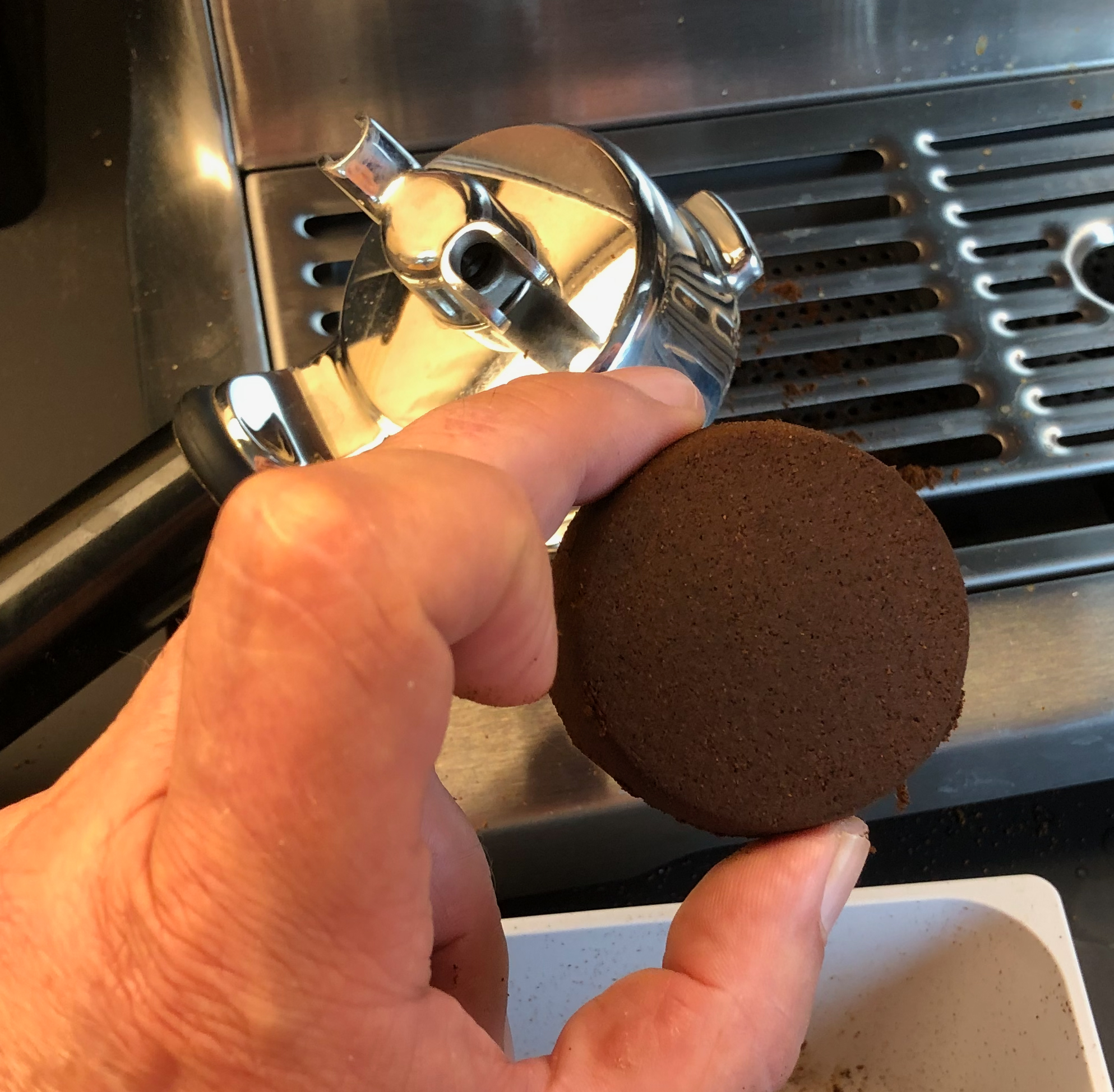 En hånd holder en kaffekake fra en espressomaskin. Foto.