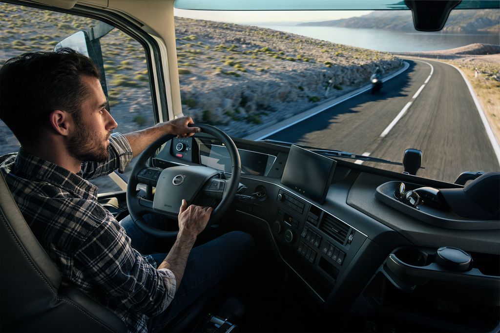 En sjåfør ved rattet. Han kjører langs en fjord. Foto.