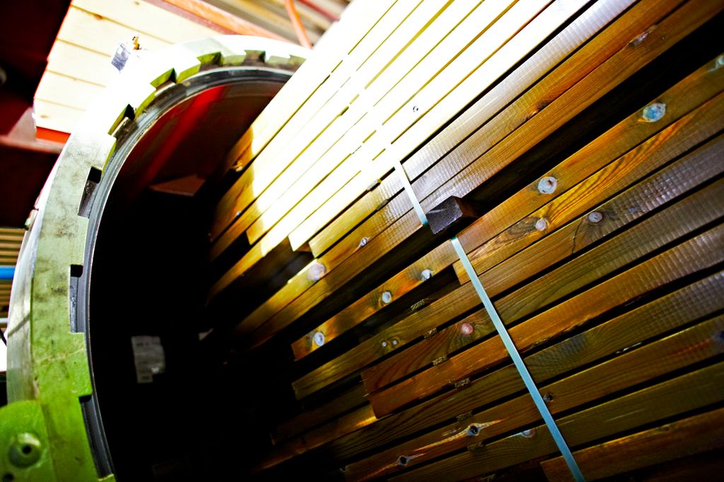 Store pakker med trelast på vei ut av et sylinderformet trykkimpregneringskammer. Foto.