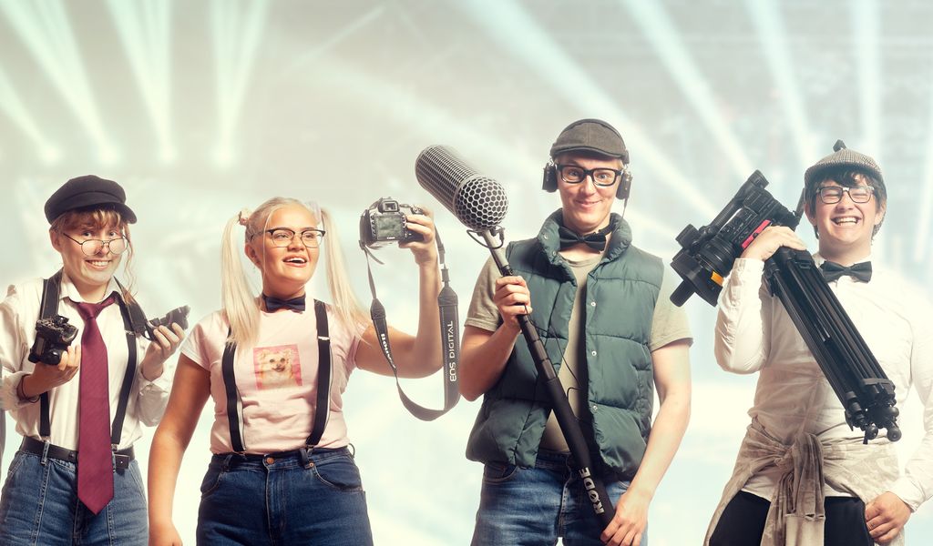 Ei gruppe ungdommer har kledd seg ut som nerder og står oppstilt på rekke med forskjellig utstyr for medieproduksjon. Foto.